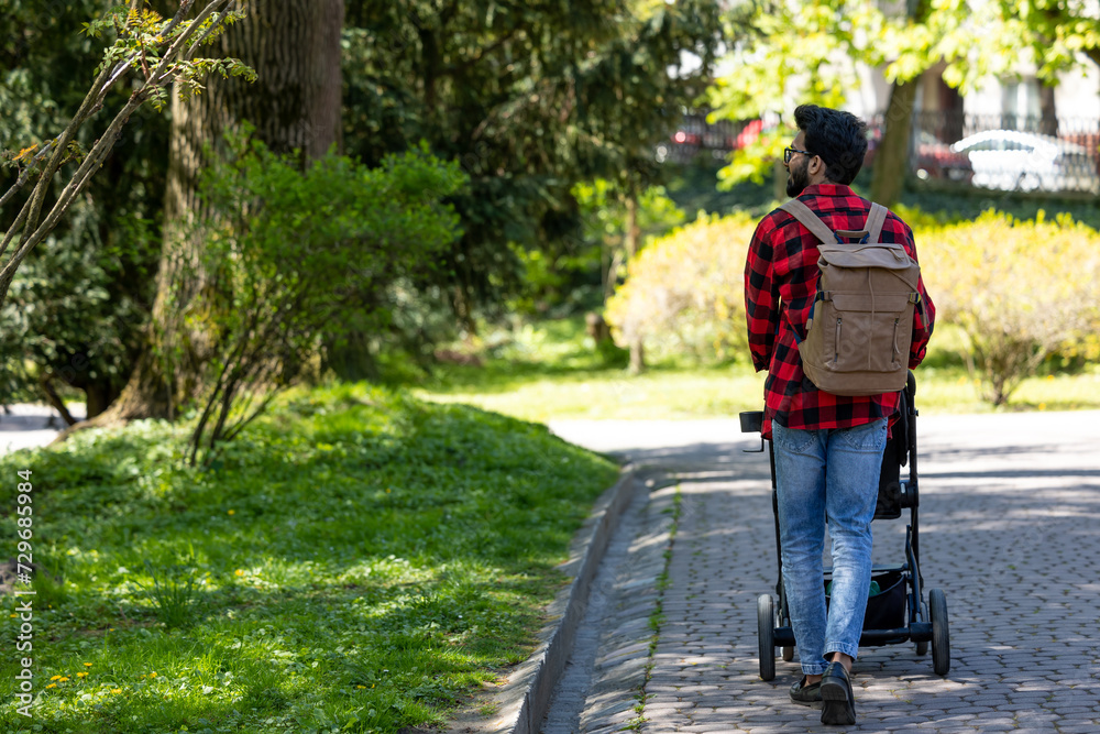 Young man in plaid shirt carrying baby carriage in the park Young man in plaid shirt carrying baby carriage in the park