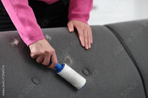 Woman with lint roller removing pet hair from sofa at home, closeup
