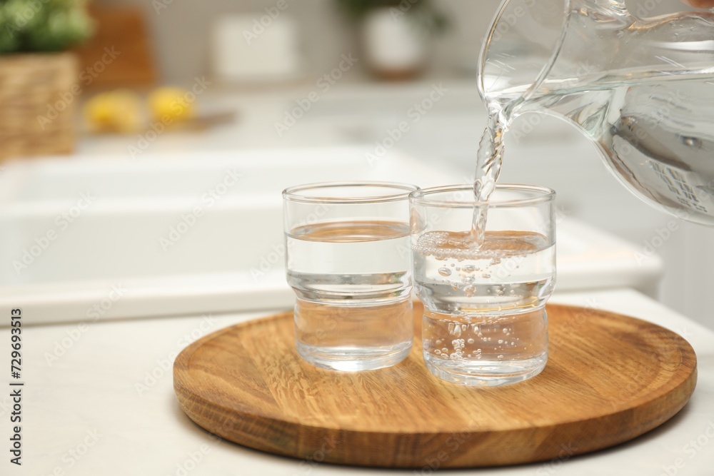 Pouring water from jug into glass on white table in kitchen, closeup. Space for text Pouring water from jug into glass on white table in kitchen, closeup. Space for text