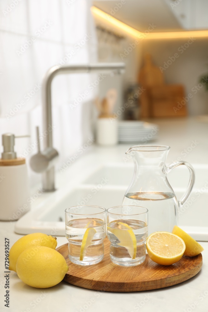 Jug, glasses with clear water and lemons on white table in kitchen Jug, glasses with clear water and lemons on white table in kitchen