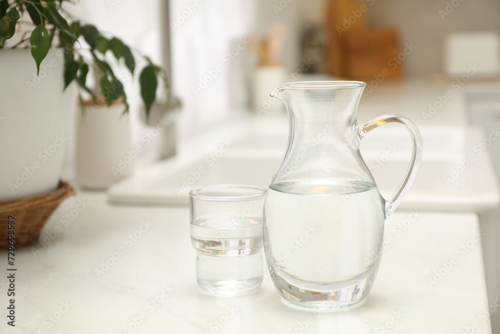 Jug and glass with clear water on white table in kitchen Jug and glass with clear water on white table in kitchen