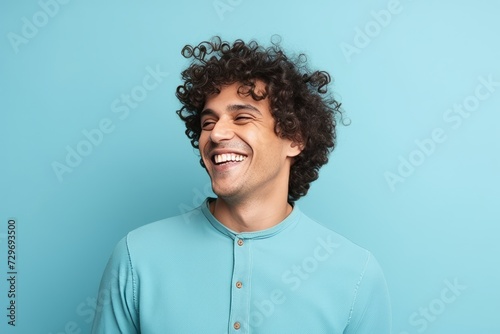 Portrait of a handsome young man with curly hair laughing against blue background