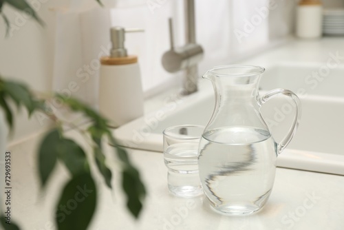 Jug and glass with clear water on white table in kitchen