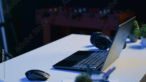Close up shot of personal office desk with laptop and headphones in dimly lit living room. Notebook and music listening device on table in empty neon illuminated apartment photo