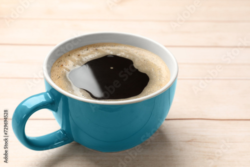Cup of aromatic coffee on light wooden table  closeup. Space for text