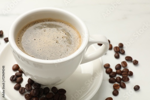 Cup of aromatic coffee and beans on white table, closeup