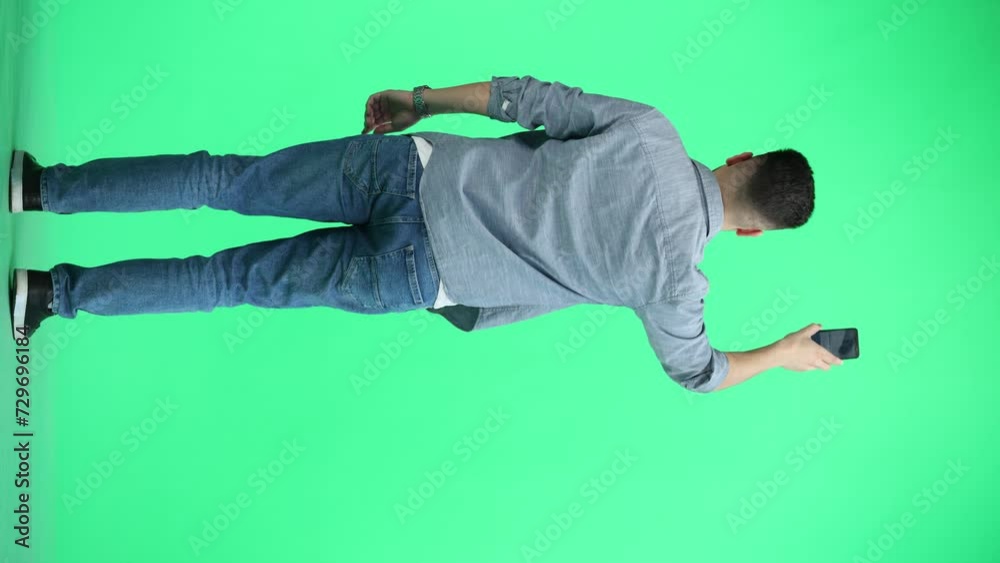 A man, full-length, on a green background, waving his phone A man, full-length, on a green background, waving his phone