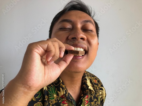 Obraz na płótnie Asian man is eating chocolate wafer w salonie