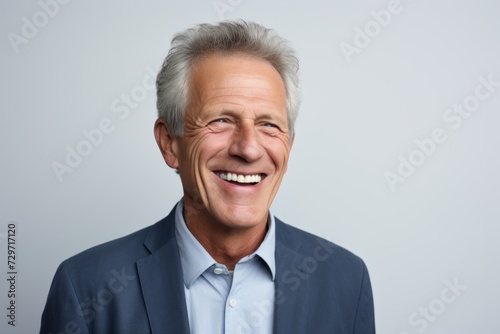 Portrait of happy senior businessman laughing and looking at camera against grey background