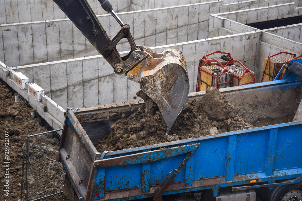 Fototapeta premium Exavator digging and unloading dirt into dump truck at construction site