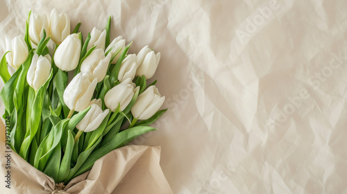 A close-up photo of a bouquet of white tulips wrapped in brown paper, lying on a clean white background