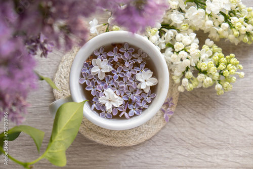Tasty black tea in white cup on windowsill with aromatic lilac flowers. Spring composition Cup of lilac tea drinking recipe flowering branches of purple lilac. Still life for copy space greeting card