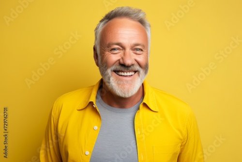 Portrait of happy senior man with grey hair and beard looking at camera on yellow background © Chacmool