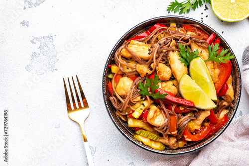 Stir fry buckwheat noodles with chicken, paprika and zucchini, ginger, garlic, sesame seed and soy saucel. White table background, top view photo