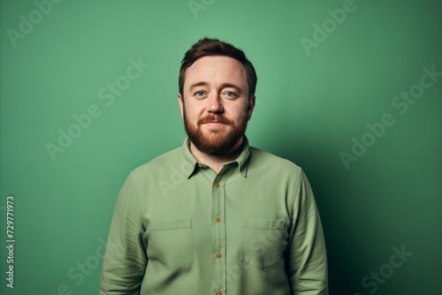 Portrait of a young bearded man in a green shirt on a green background.