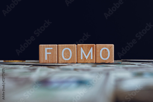 Wooden blocks with the text "FOMO" on a black background and crypto banknotes scattered on the ground.