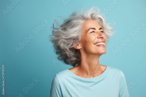 Happy senior woman laughing and looking up on blue background with copy space