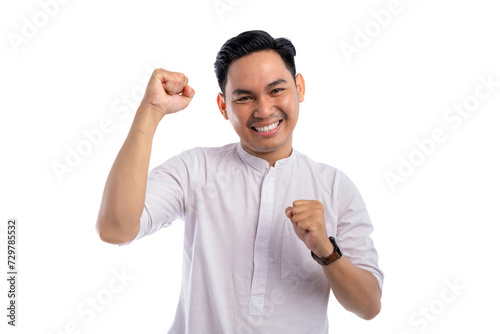 Happy Asian Muslim man celebrating success with raised fist isolated on white background. Ramadan and Eid Fitr celebration concept