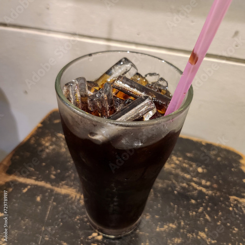 A glass of iced coffee with a pink straw on a wooden table.