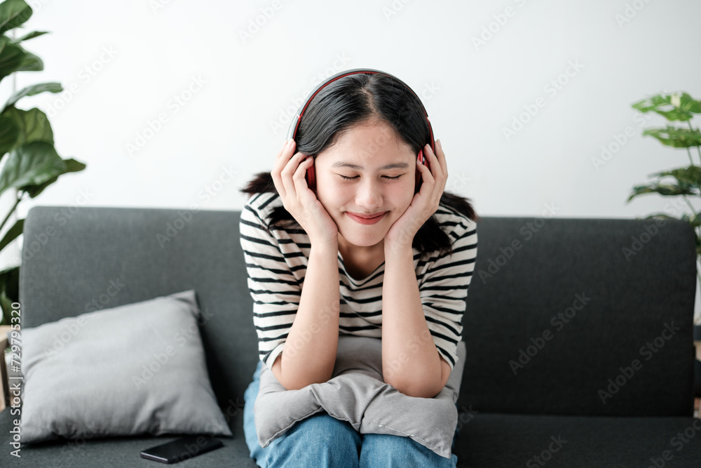 Attractive and happy young Asian woman in casual clothes wearing headphones, relaxes listening to music in her home office. Attractive and happy young Asian woman in casual clothes wearing headphones, relaxes listening to music in her home office.