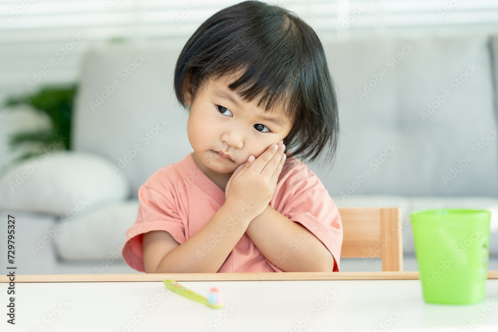 little asian girl presses hand to cheek, suffers from pain in tooth. Teeth decay, dental problems, child emotions and facial expression, oral health care, reducing sweets, fluorine coating little asian girl presses hand to cheek, suffers from pain in tooth. Teeth decay, dental problems, child emotions and facial expression, oral health care, reducing sweets, fluorine coating