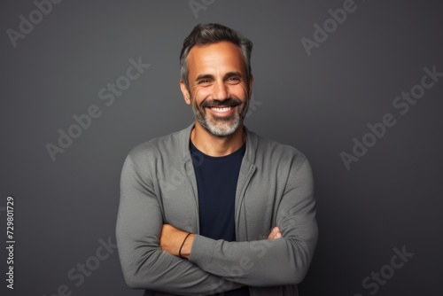 Handsome middle-aged man smiling and looking at camera while standing against grey background © Inigo