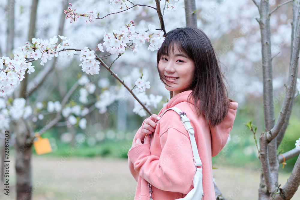 Beautiful young Chinese woman smiling under blooming cherry tree, wearing pink loose oversized top with small white shoulder bag. Candid moment. Emotions, people, beauty, youth and lifestyle portrait. Beautiful young Chinese woman smiling under blooming cherry tree, wearing pink loose oversized top with small white shoulder bag. Candid moment. Emotions, people, beauty, youth and lifestyle portrait.