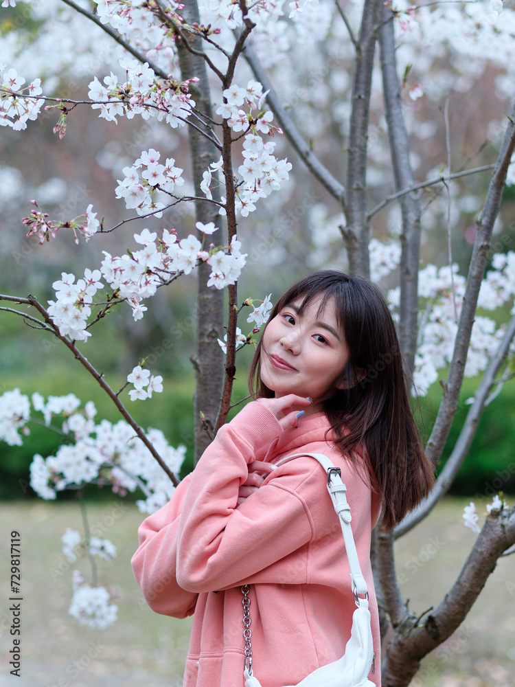 Beautiful young Chinese woman smiling under blooming cherry tree, wearing pink loose oversized top with small white shoulder bag. Candid moment. Emotions, people, beauty, youth and lifestyle portrait. Beautiful young Chinese woman smiling under blooming cherry tree, wearing pink loose oversized top with small white shoulder bag. Candid moment. Emotions, people, beauty, youth and lifestyle portrait.