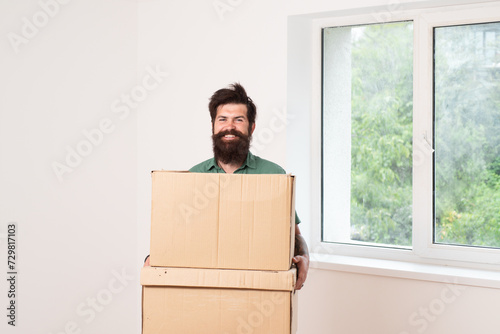 Happy cheerful man carrying cardboard box on moving day. Delivery man loading cardboard boxes for moving to an apartment. © Volodymyr