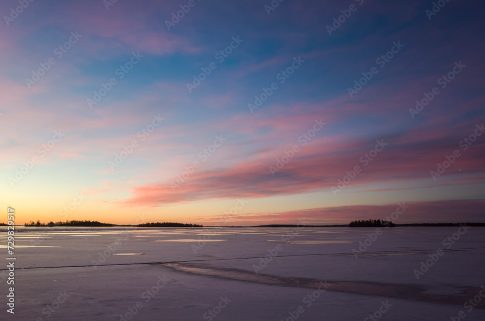 Glowing pink and yellow morning sky over frozen lake Mälaren at sunrise, Västerås, winter in Sweden