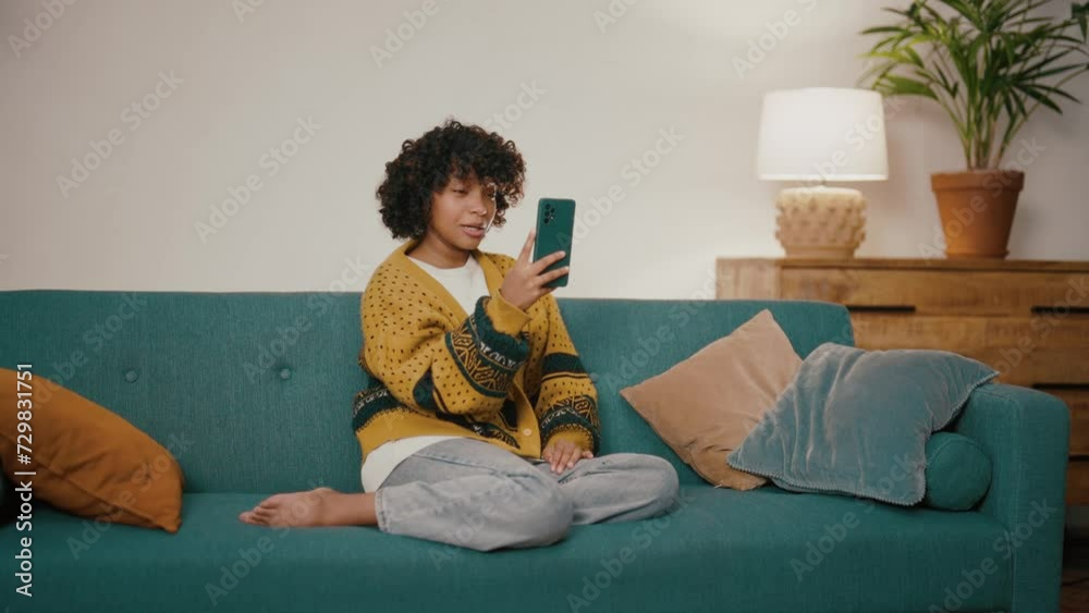 Young woman with phone talking with friends family. African American girl hold in hand use mobile phone. Teenager relax spend spare time in living room with phone. Communication on social networks. Young woman with phone talking with friends family. African American girl hold in hand use mobile phone. Teenager relax spend spare time in living room with phone. Communication on social networks.