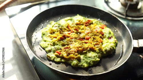 Green pancake or indian chilla prepared on black pan in kitchen with sunlight photo