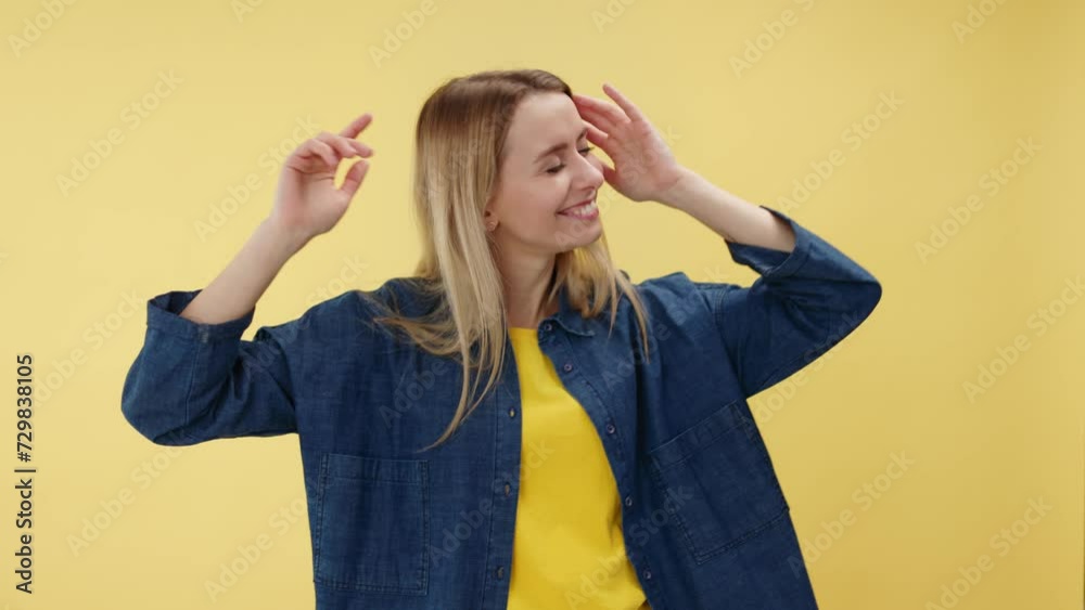 Portrait of cheerful attractive woman dancing and having fun with raising hands up against isolated yellow background. Lady dressed in denim casual jacket expressing happiness in studio setting. Portrait of cheerful attractive woman dancing and having fun with raising hands up against isolated yellow background. Lady dressed in denim casual jacket expressing happiness in studio setting.