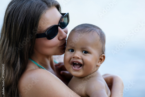 Close up portrait of mother kissing multiracial baby. Mom kiss Biracial child. Closeup face of Mother with Biracial baby kissing outdoor. Tender moms kiss. Biracial or multiracial baby and mom kissed.