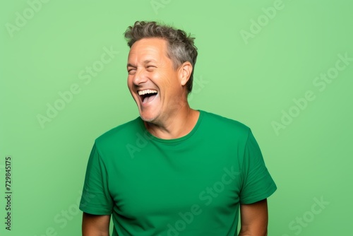 Handsome mature man laughing and looking at the camera over green background
