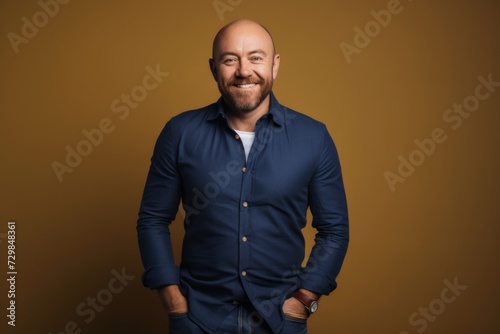 Handsome bald man in a blue shirt is posing on a brown background