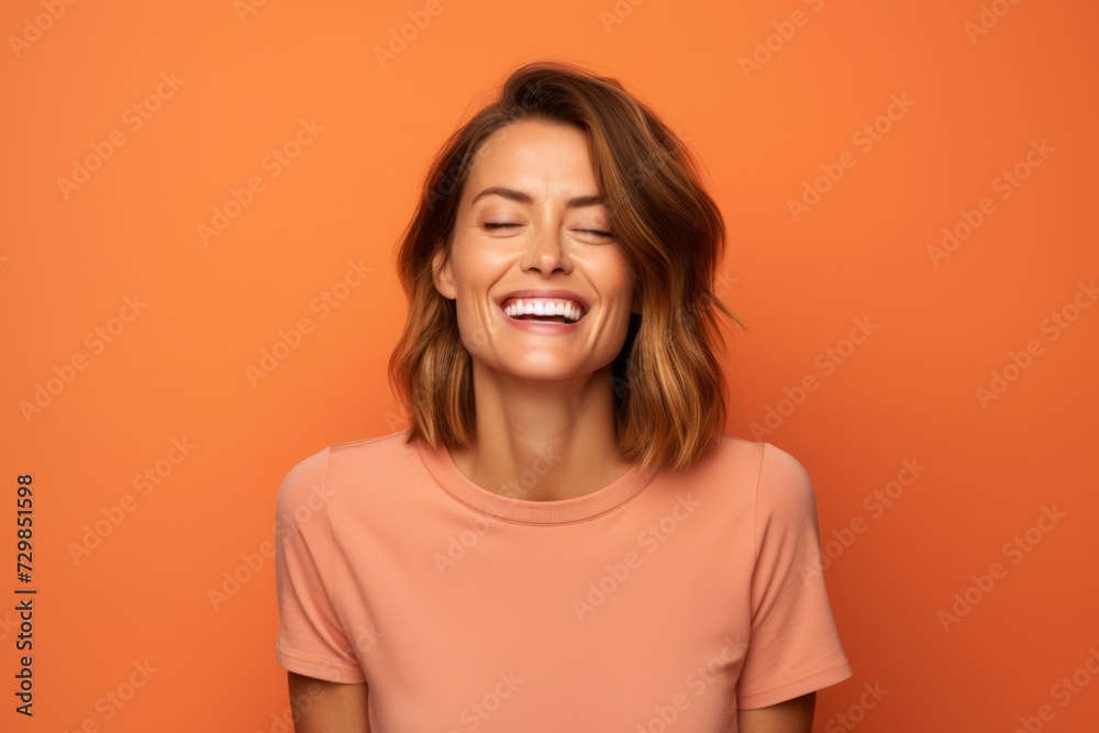 Portrait of a happy young woman laughing with closed eyes on orange background Portrait of a happy young woman laughing with closed eyes on orange background