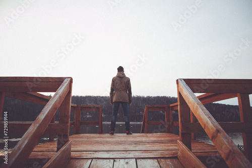 A Man Is Standing On A Wooden Dock Overlooking A Lake