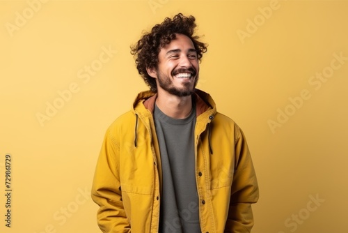 Handsome man with curly hair laughing and looking to the side on yellow background © Inigo