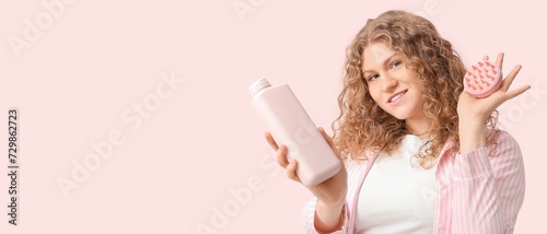 Beautiful young woman with hair scalp massager and shampoo on pink background with space for text photo