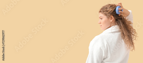 Beautiful young woman using hair scalp massager on beige background with space for text