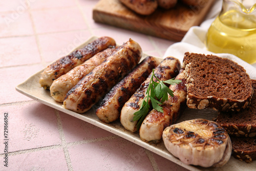 Plate of tasty grilled sausages and bread on pink tile background