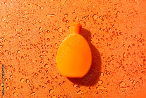Bottle of sunscreen cream with water drops on orange background