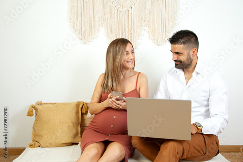 Pareja de enamorados comprando desde el portatil de su casa. Futuros padres haciendo la compra. Embarazo. Tecnología