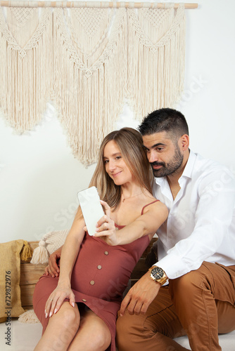 Pareja de enamorados haciéndose una foto en su casa. Futuros padres haciendose un selfie. Embarazo. Tecnología