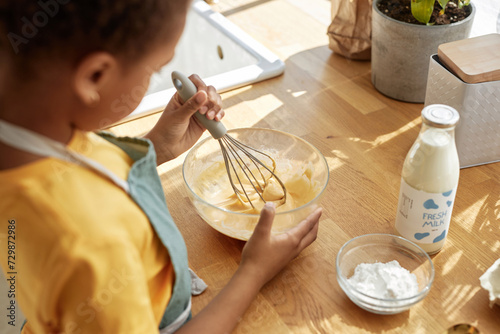 High angle view selective focus of unrecognizable Black kid mixing ingredients for pancakes in glass bowl photo