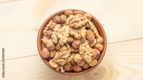 Mixed nuts in a clay cup on a wooden table, walnut kernels, peeled dried hazelnuts, almonds and cashews, top view, healthy and wholesome food concept