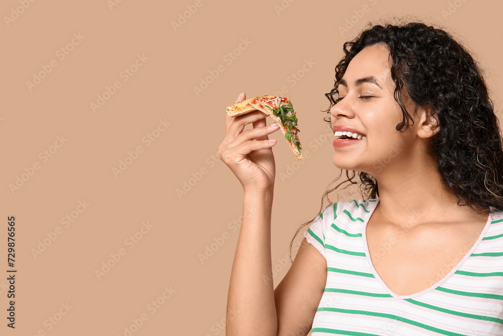 Beautiful young happy African-American woman with slice of delicious pizza on beige background