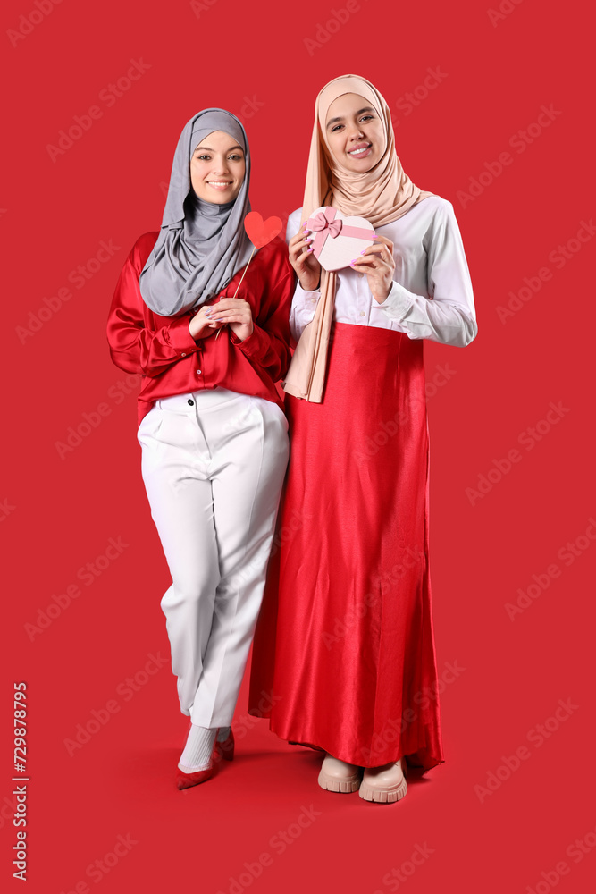 Young Muslim women in hijab with gift box on red background