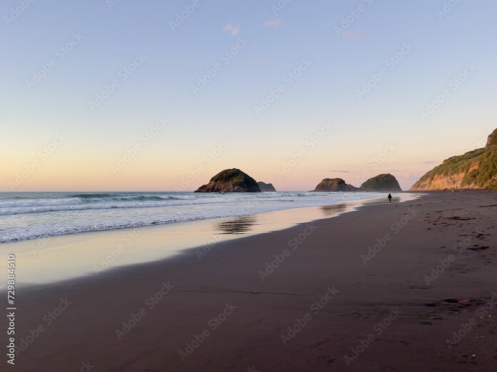 Woman walking away in the distance along an isolated west coast beach in New Zealand at sunset